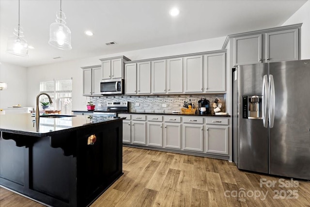 kitchen with stainless steel appliances, backsplash, gray cabinetry, light wood-style floors, and a sink