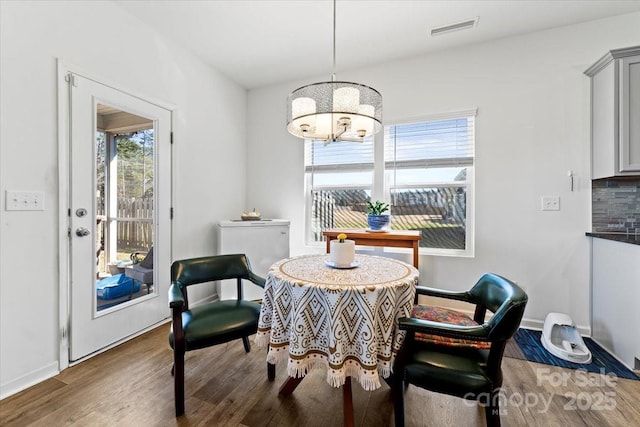 dining space featuring visible vents, a notable chandelier, baseboards, and wood finished floors