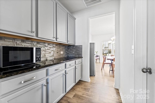 kitchen featuring visible vents, baseboards, light wood-style floors, backsplash, and dark stone countertops