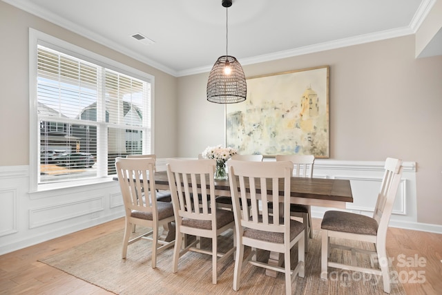 dining space featuring light wood-style floors, wainscoting, visible vents, and crown molding