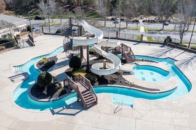 pool featuring a water slide, playground community, fence, and a water play area