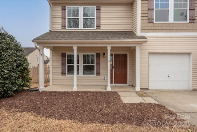 view of front of home with driveway, a shingled roof, an attached garage, fence, and a porch