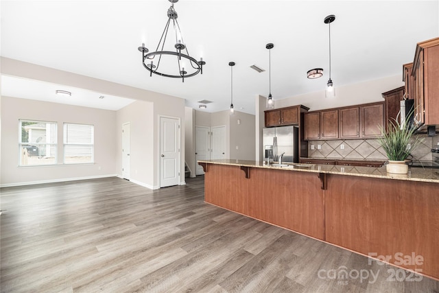 kitchen with stainless steel fridge, light stone counters, a breakfast bar, a peninsula, and backsplash