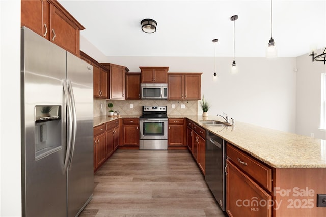 kitchen featuring stainless steel appliances, backsplash, a sink, wood finished floors, and a peninsula