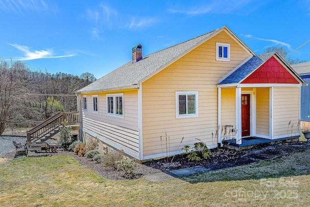 exterior space with a shingled roof, a yard, and a chimney