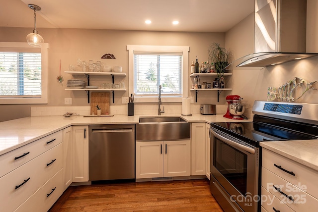 kitchen featuring open shelves, light countertops, appliances with stainless steel finishes, a sink, and wall chimney exhaust hood