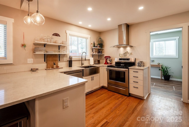 kitchen featuring wall chimney exhaust hood, appliances with stainless steel finishes, light wood-style floors, open shelves, and a sink