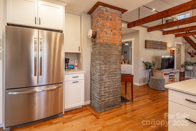 kitchen with baseboards, white cabinets, light countertops, stainless steel refrigerator, and light wood finished floors