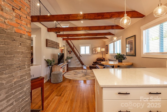 kitchen with vaulted ceiling with beams, light countertops, hanging light fixtures, white cabinets, and light wood-type flooring