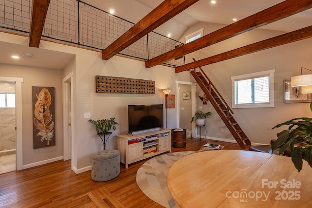 living area featuring stairs, beamed ceiling, baseboards, and wood finished floors