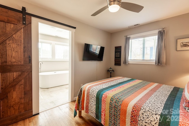 bedroom with a ceiling fan, wood finished floors, visible vents, and a barn door