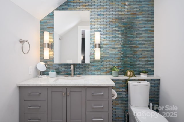 bathroom featuring backsplash, vanity, toilet, and vaulted ceiling