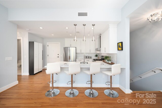 kitchen featuring a peninsula, stainless steel appliances, white cabinetry, a kitchen breakfast bar, and tasteful backsplash