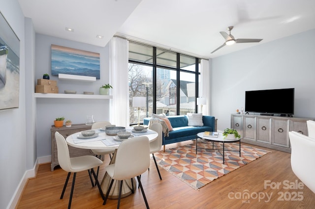 dining area with light wood-style flooring, a wall of windows, baseboards, and ceiling fan