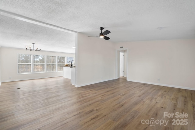 unfurnished room featuring baseboards, light wood-style flooring, a textured ceiling, and ceiling fan with notable chandelier