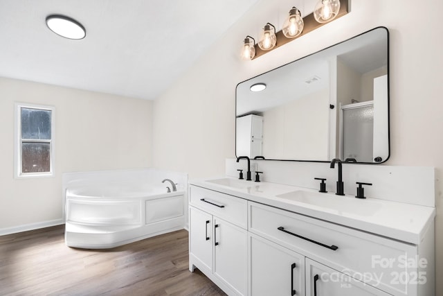 full bath with double vanity, a garden tub, a sink, and wood finished floors