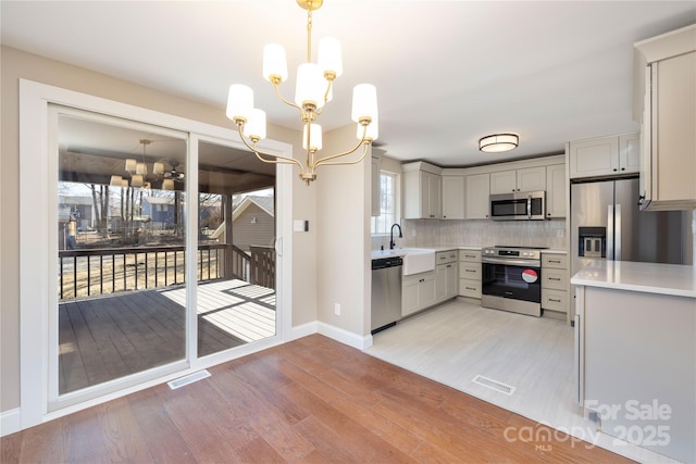 kitchen with a notable chandelier, light countertops, appliances with stainless steel finishes, light wood-type flooring, and tasteful backsplash