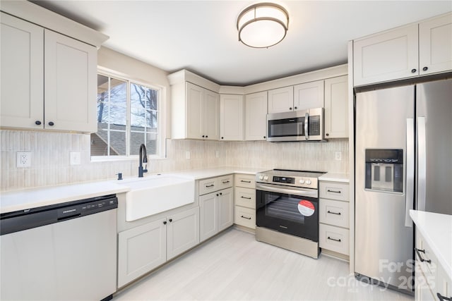 kitchen featuring appliances with stainless steel finishes, light countertops, a sink, and backsplash