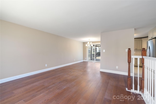 spare room with dark wood finished floors, a notable chandelier, and baseboards