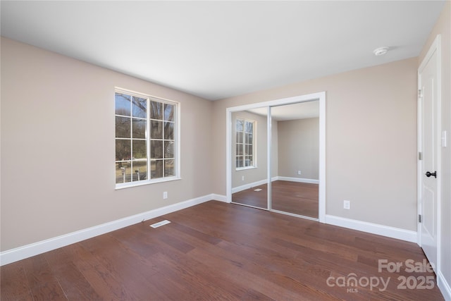 unfurnished bedroom featuring a closet, visible vents, baseboards, and wood finished floors