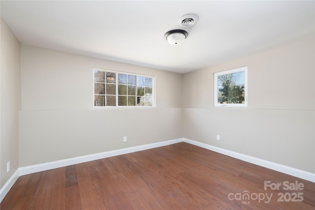 spare room with wood finished floors, visible vents, and baseboards