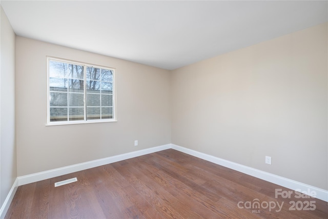 unfurnished room with dark wood-style floors, visible vents, and baseboards