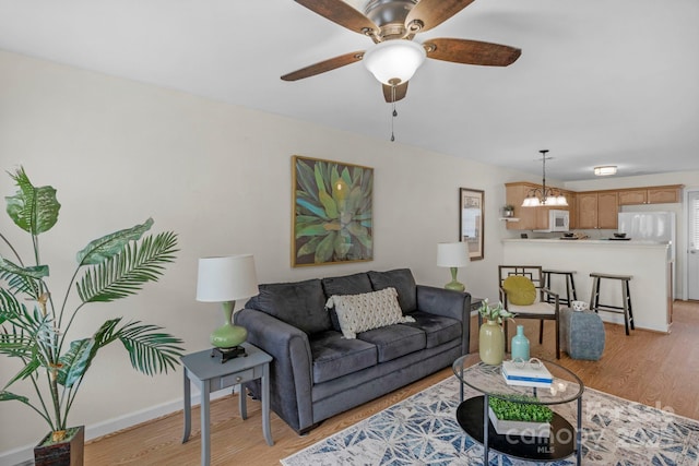 living room with light wood-type flooring, baseboards, and ceiling fan with notable chandelier