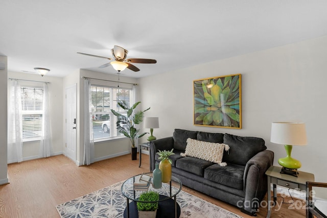 living area featuring a ceiling fan, light wood-style flooring, and baseboards