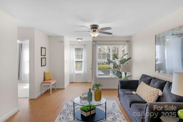 living area with light wood-style floors, ceiling fan, and baseboards