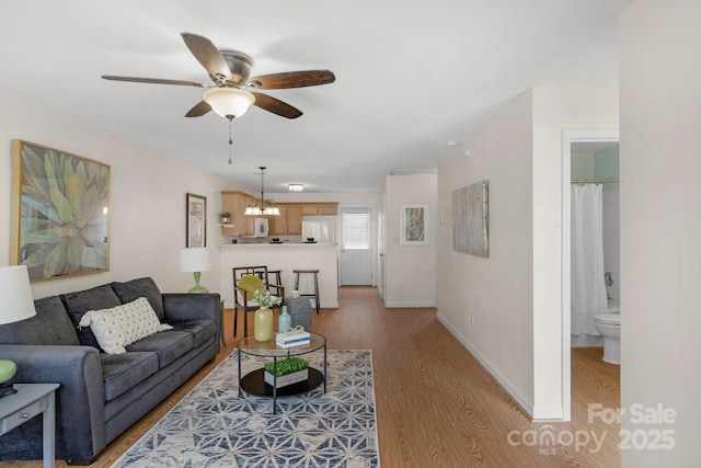 living area with light wood-style flooring, baseboards, and ceiling fan with notable chandelier