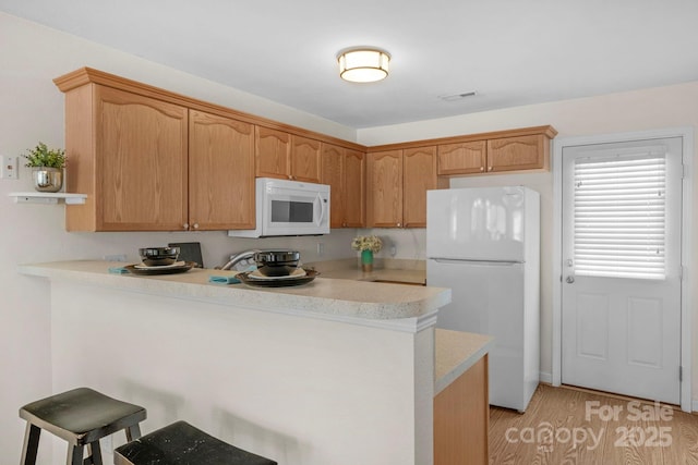 kitchen featuring white appliances, a kitchen breakfast bar, a peninsula, light countertops, and light wood-type flooring