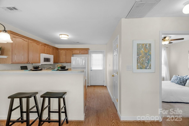 kitchen with a peninsula, white microwave, a breakfast bar, and visible vents