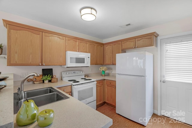 kitchen with white appliances, light wood finished floors, visible vents, light countertops, and a sink