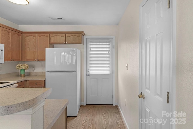 kitchen with white appliances, visible vents, baseboards, light wood-style floors, and light countertops