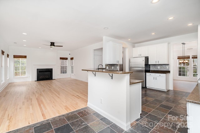 kitchen with stone tile floors, a peninsula, a breakfast bar, white cabinets, and freestanding refrigerator