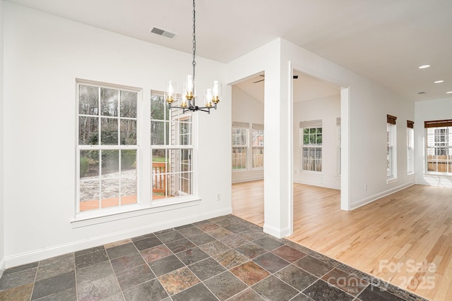 unfurnished dining area featuring stone tile flooring, visible vents, baseboards, and an inviting chandelier