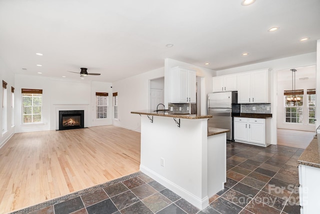 kitchen with a breakfast bar area, stone tile floors, a peninsula, white cabinets, and freestanding refrigerator