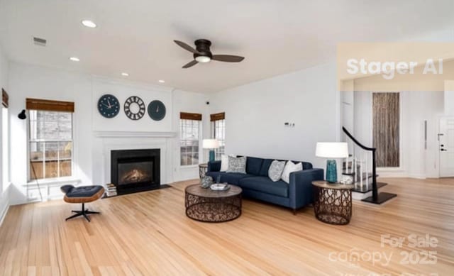 living room featuring visible vents, a fireplace with flush hearth, a ceiling fan, wood finished floors, and stairs