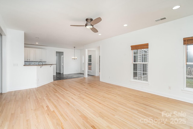 unfurnished living room with light wood-style floors, recessed lighting, visible vents, and ceiling fan with notable chandelier