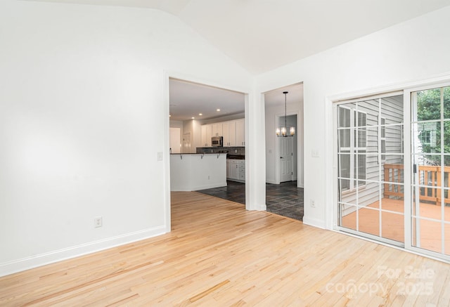 unfurnished room with light wood-type flooring, vaulted ceiling, baseboards, and an inviting chandelier