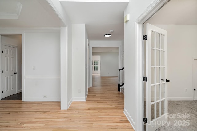 hall featuring light wood-type flooring, crown molding, and baseboards