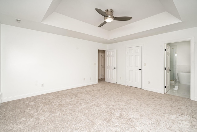 unfurnished bedroom featuring light carpet, ensuite bath, baseboards, and a raised ceiling