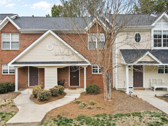 townhome / multi-family property featuring brick siding, covered porch, and roof with shingles