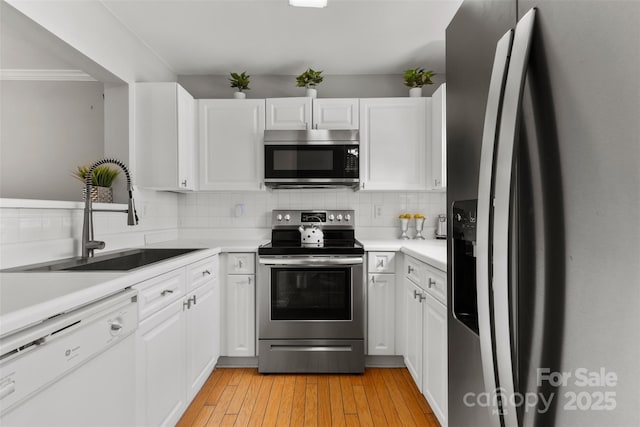 kitchen featuring a sink, stainless steel appliances, white cabinets, tasteful backsplash, and light wood-type flooring