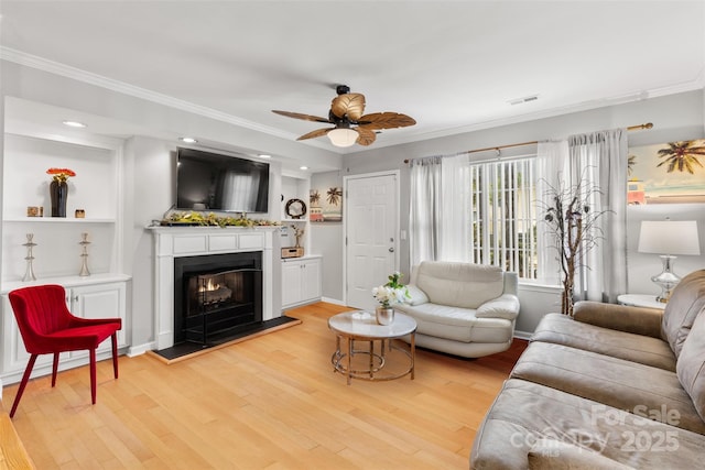 living area with light wood-style flooring, crown molding, and a lit fireplace