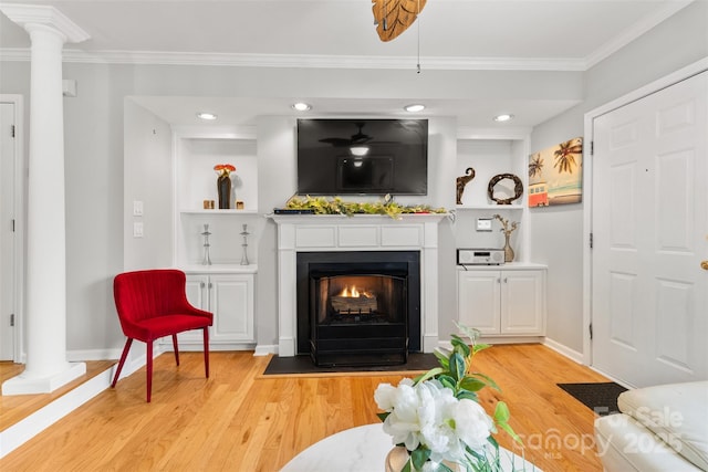 living area featuring crown molding, a fireplace with flush hearth, light wood-type flooring, and ornate columns