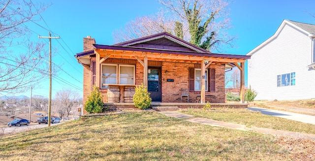 view of front of house featuring covered porch, brick siding, a chimney, and a front yard