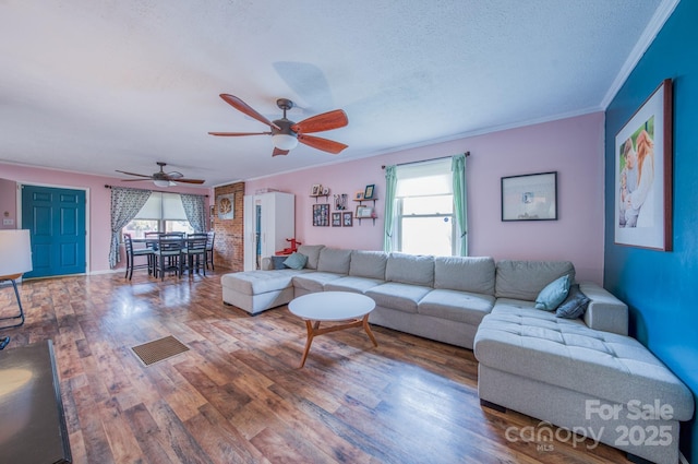 living area with ornamental molding, ceiling fan, a textured ceiling, and wood finished floors