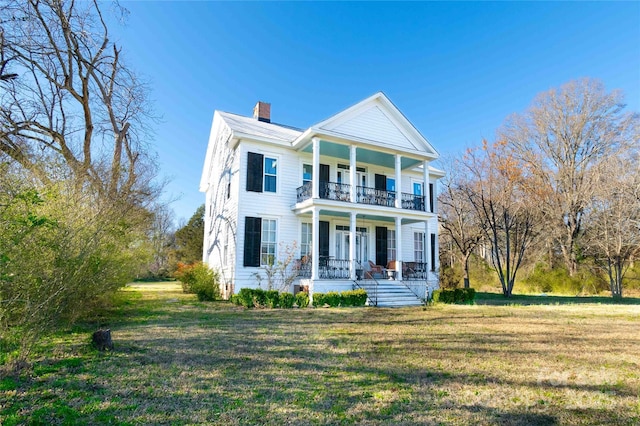 greek revival inspired property with a chimney, a porch, a front yard, and a balcony