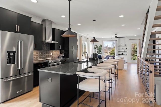 kitchen featuring high end appliances, wall chimney exhaust hood, a breakfast bar area, dark cabinets, and a sink